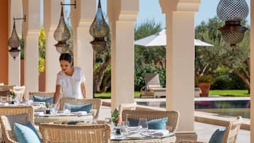 A well-appointed outdoor dining area with wicker furniture and hanging lanterns, overlooking a pool and greenery.