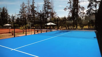 An outdoor tennis court with a blue surface, surrounded by trees and a fence.