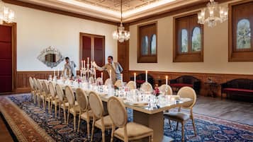 A formal dining room with a long table set for a meal, chandeliers, and large windows with views.