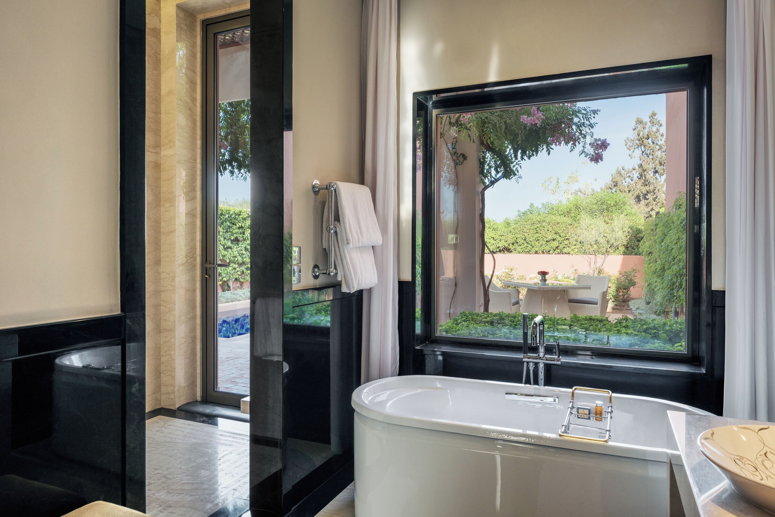 A modern bathroom with a freestanding bathtub, a glass shower enclosure, and a view of a garden through a large window.