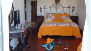 A bedroom with a wooden bed, an orange bedspread, a chandelier, and a desk with a mirror. - Casa Celeste Sperlongaresort (Sperlonga)