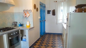 A compact kitchen with a gas stove, oven, and a refrigerator. - Casa Celeste Sperlongaresort (Sperlonga)