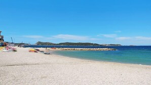 A beach with a rocky breakwater, clear blue water, and a sandy shore.