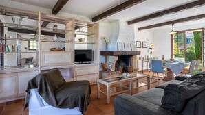 A cozy living room with a fireplace, wooden beams, and a dining area with a table and chairs.