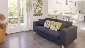 Een moderne woonkamer met een donkergrijze bank, een rieten mand en een groot raam met gordijnen.