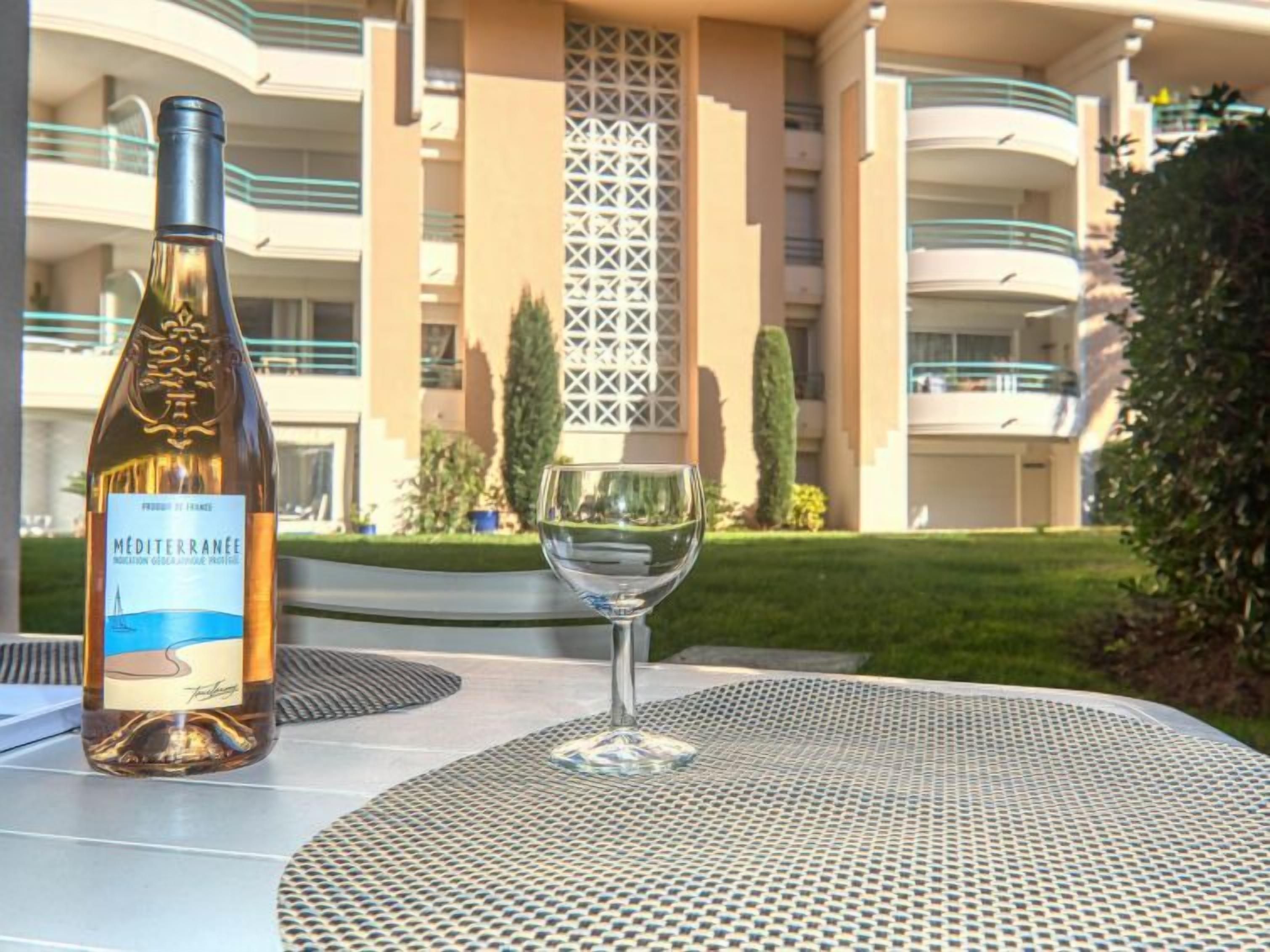 A bottle of wine and a glass on a table with a view of a multi-story building with balconies.
