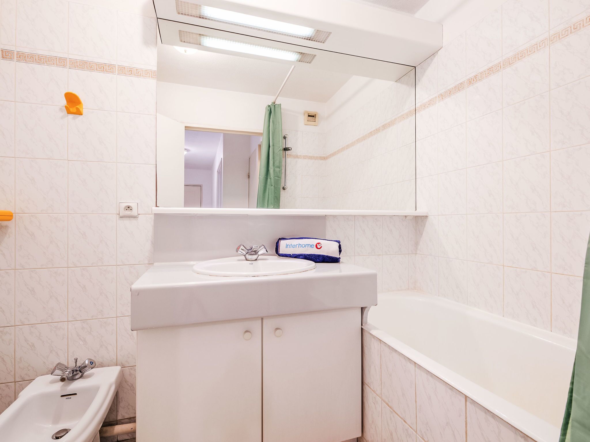 A bathroom with a white sink, mirror, and bathtub. There is a green shower curtain and a white towel hanging on the wall.