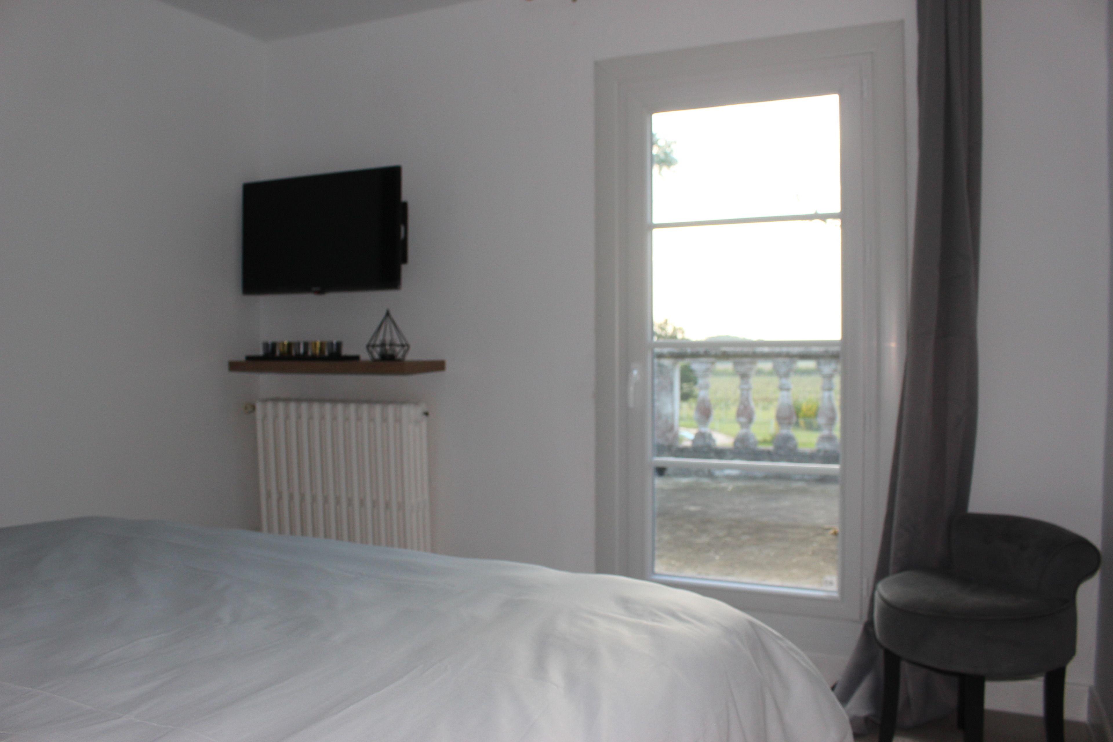 A bedroom with a bed, a television mounted on the wall, a window with curtains, and a chair.