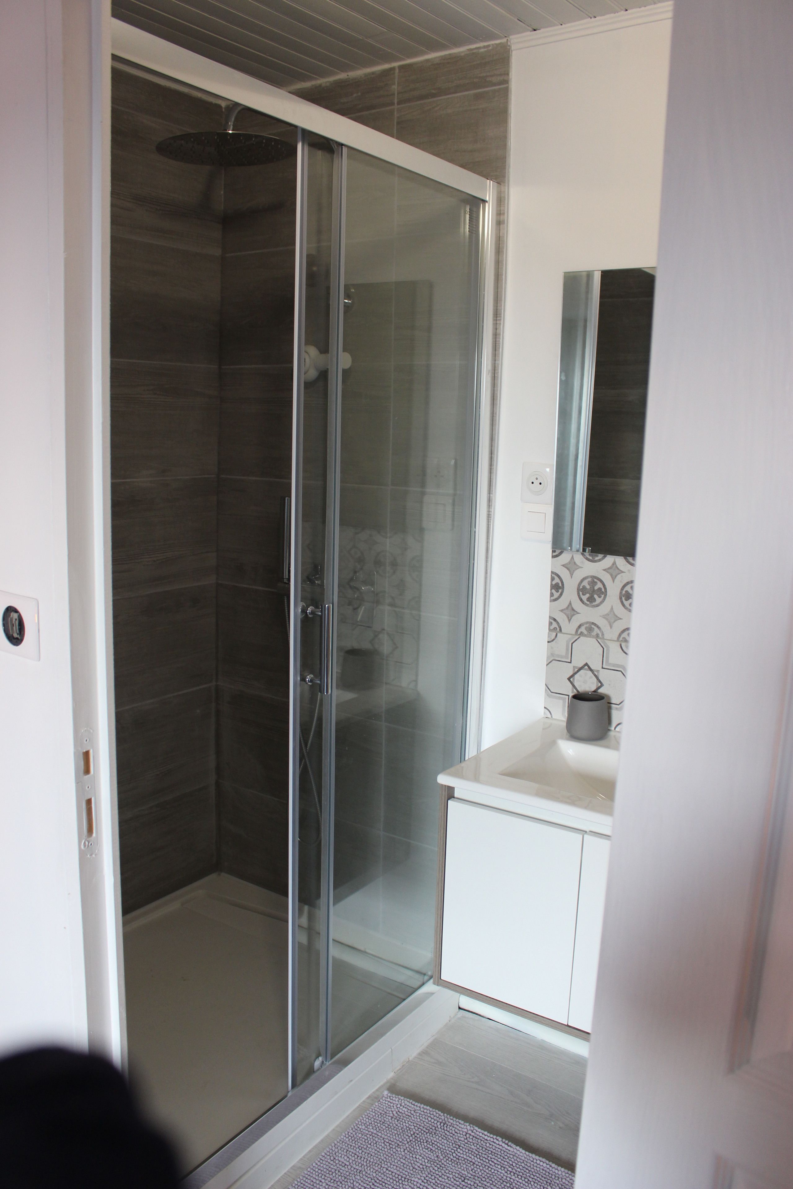 Une salle de bain avec une douche à parois de verre, un lavabo blanc et un miroir au-dessus.