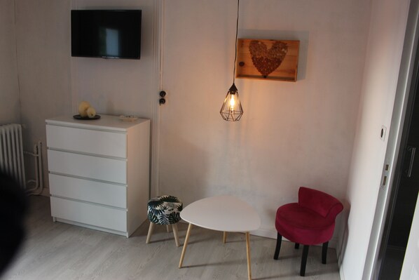 A small, well-lit room with a white dresser, a red chair, a small table, a wall-mounted TV, and a unique heart-shaped wooden shelf. - Chateau la Loge (Villematier)
