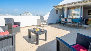 A rooftop patio with wicker furniture, a small table with cups, and a view of the sea and buildings. - Cap Sud by Interhome (La Grande Motte)