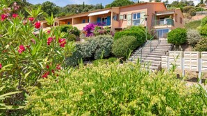 A two-story building with a staircase leading to the entrance, surrounded by lush greenery and flowering plants. - Les Hauts des Issambres by Interhome (Les Issambres)