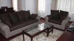 A living room with two sofas, a glass coffee table, and a patterned rug. - Angel Court Apartments (Nairobi)