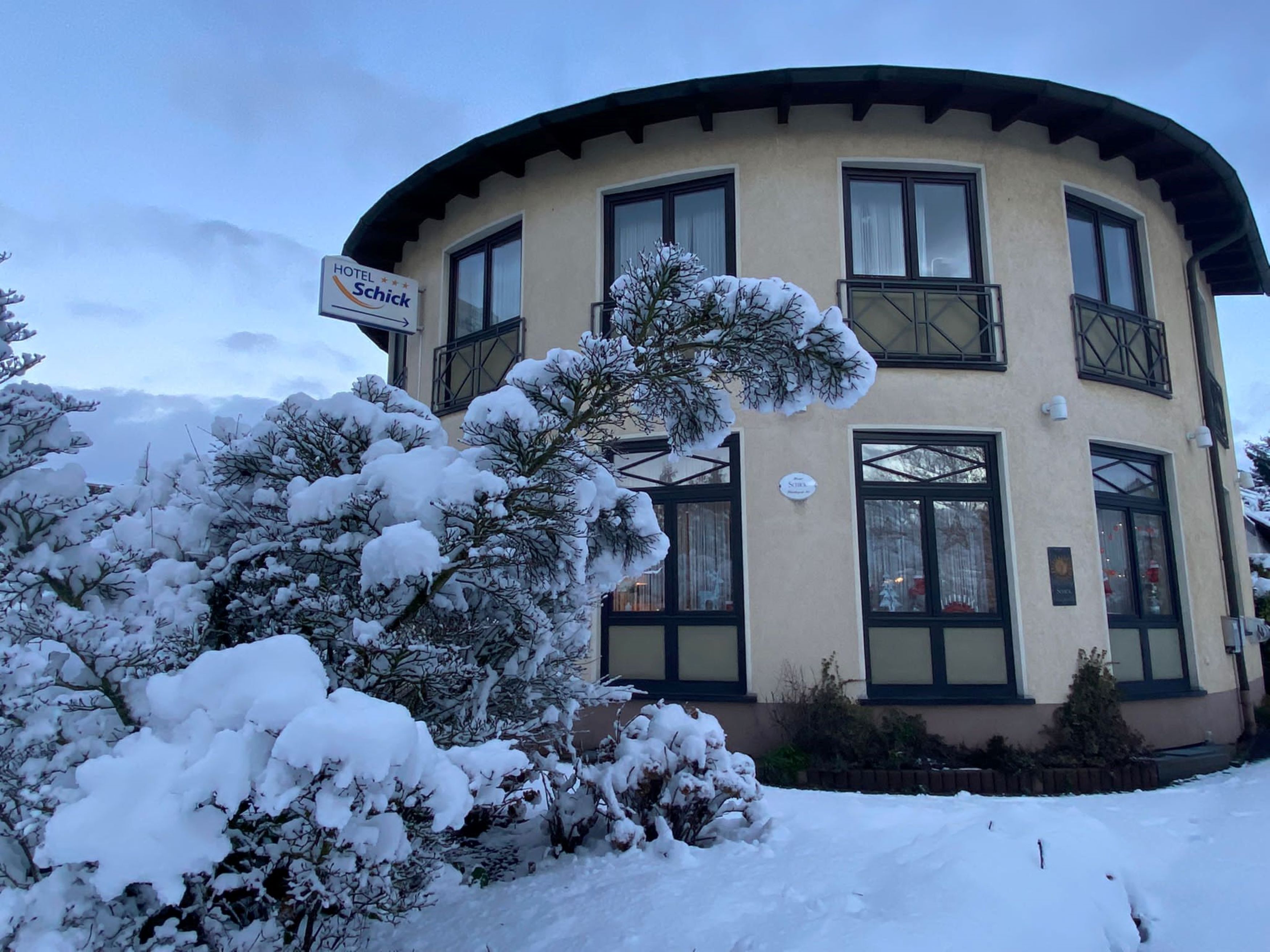 Un hotel llamado 'Hotel Schick' con una fachada curva, múltiples ventanas y alrededores cubiertos de nieve.
