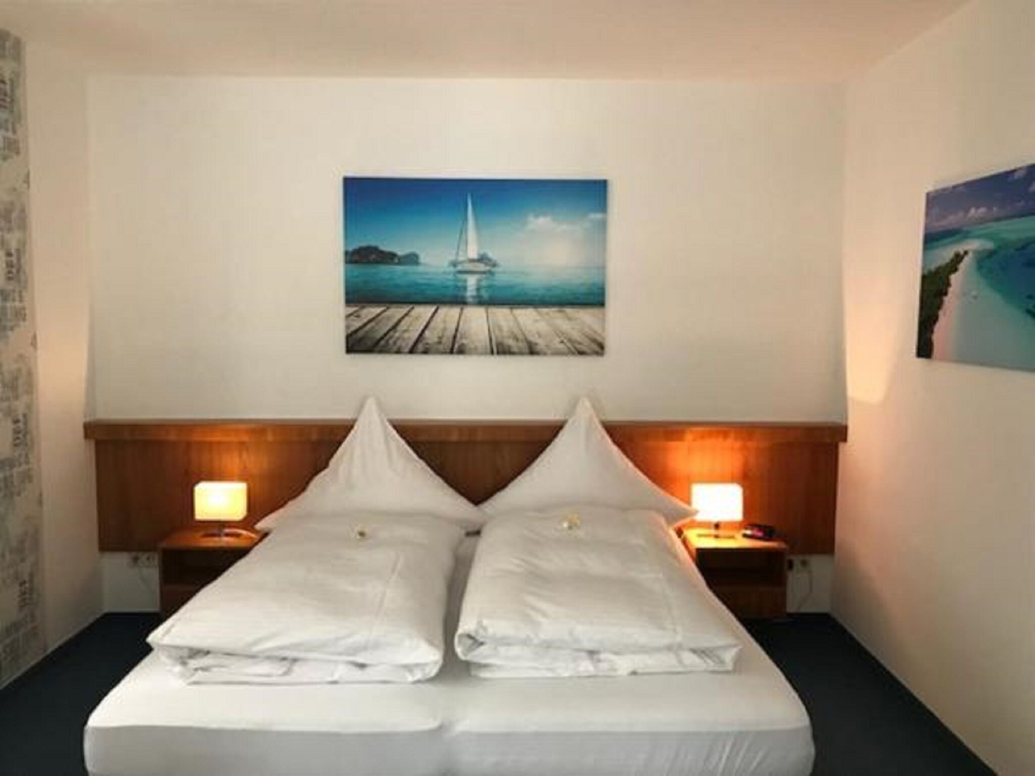 A hotel room with a bed, two bedside tables, and a painting of a pier and water on the wall.