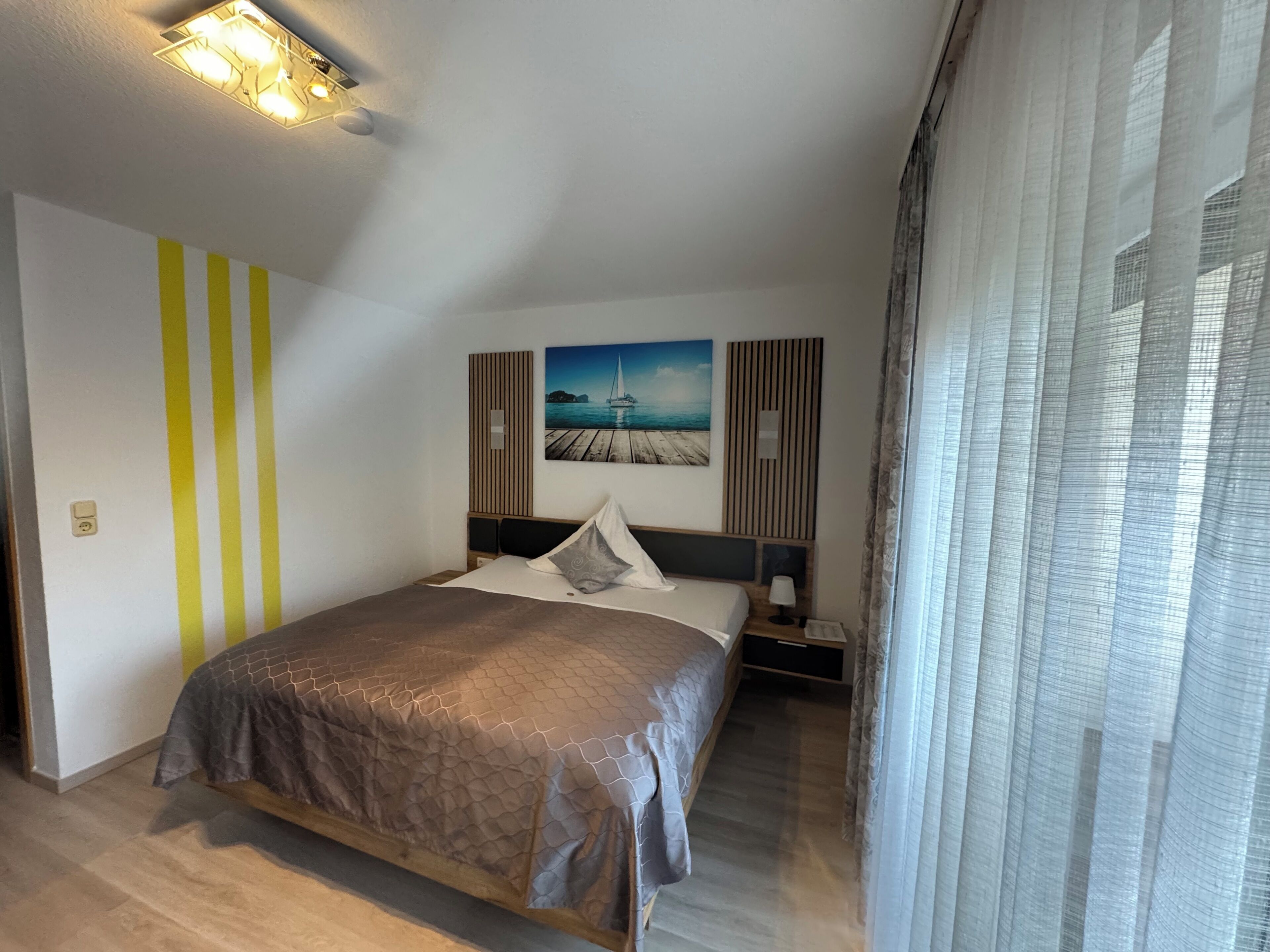 Ett modernt hotellrum med en stor säng, en tavla som föreställer ett kustlandskap och en taklampa.