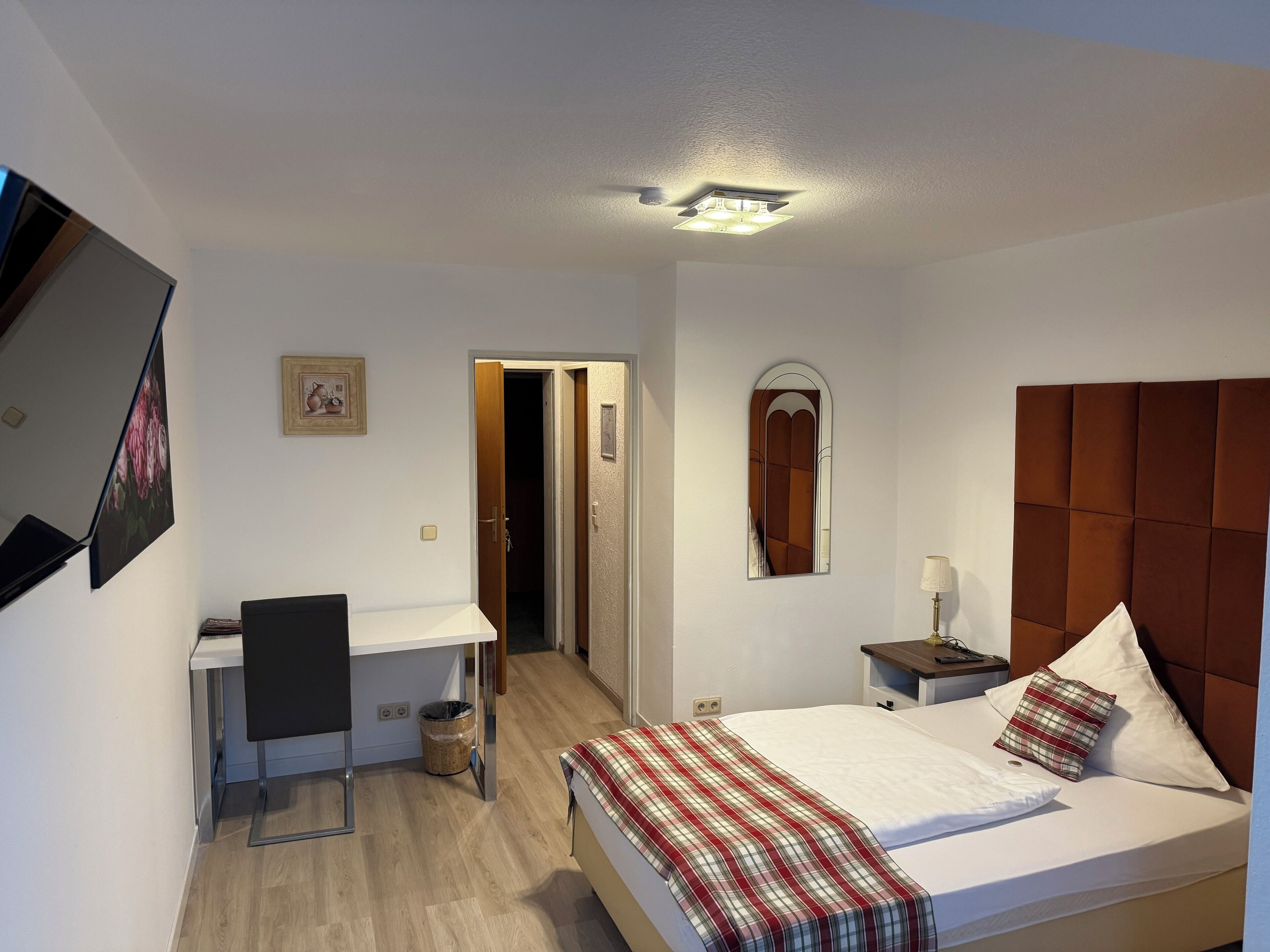 A hotel room with a bed, a desk, a chair, a nightstand, and a mirror.