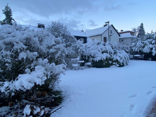 A snow-covered garden with a patio area and a house in the background. - Hotel Schick (Oberursel)