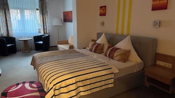 A hotel room with a large bed, a small round table, two armchairs, a sofa, and a window with curtains.