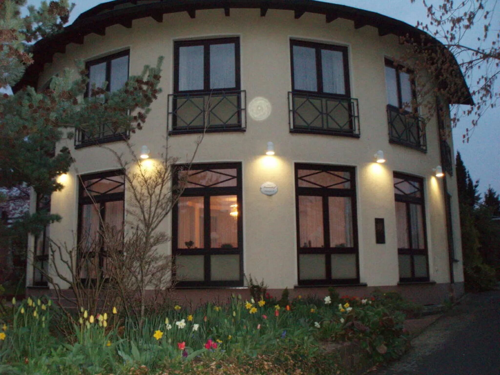 Un edificio de varios pisos con balcones, ventanas grandes y un jardín con diversas flores.