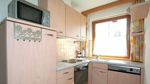 A compact kitchen with wooden cabinets, a microwave, a stove, and a sink. - Herbert by Interhome (Kaltenbach)
