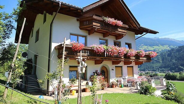 A two-story chalet with a balcony adorned with flowers, set against a mountainous backdrop. - Herbert by Interhome (Kaltenbach)