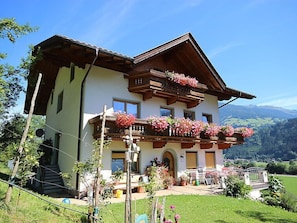 A two-story chalet with a balcony adorned with flowers, set against a mountainous backdrop. - Herbert by Interhome (Kaltenbach)