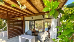 Un espace extérieur aménagé en terrasse, avec un plafond en bois, une table blanche, deux chaises et une porte vitrée donnant sur un espace intérieur.