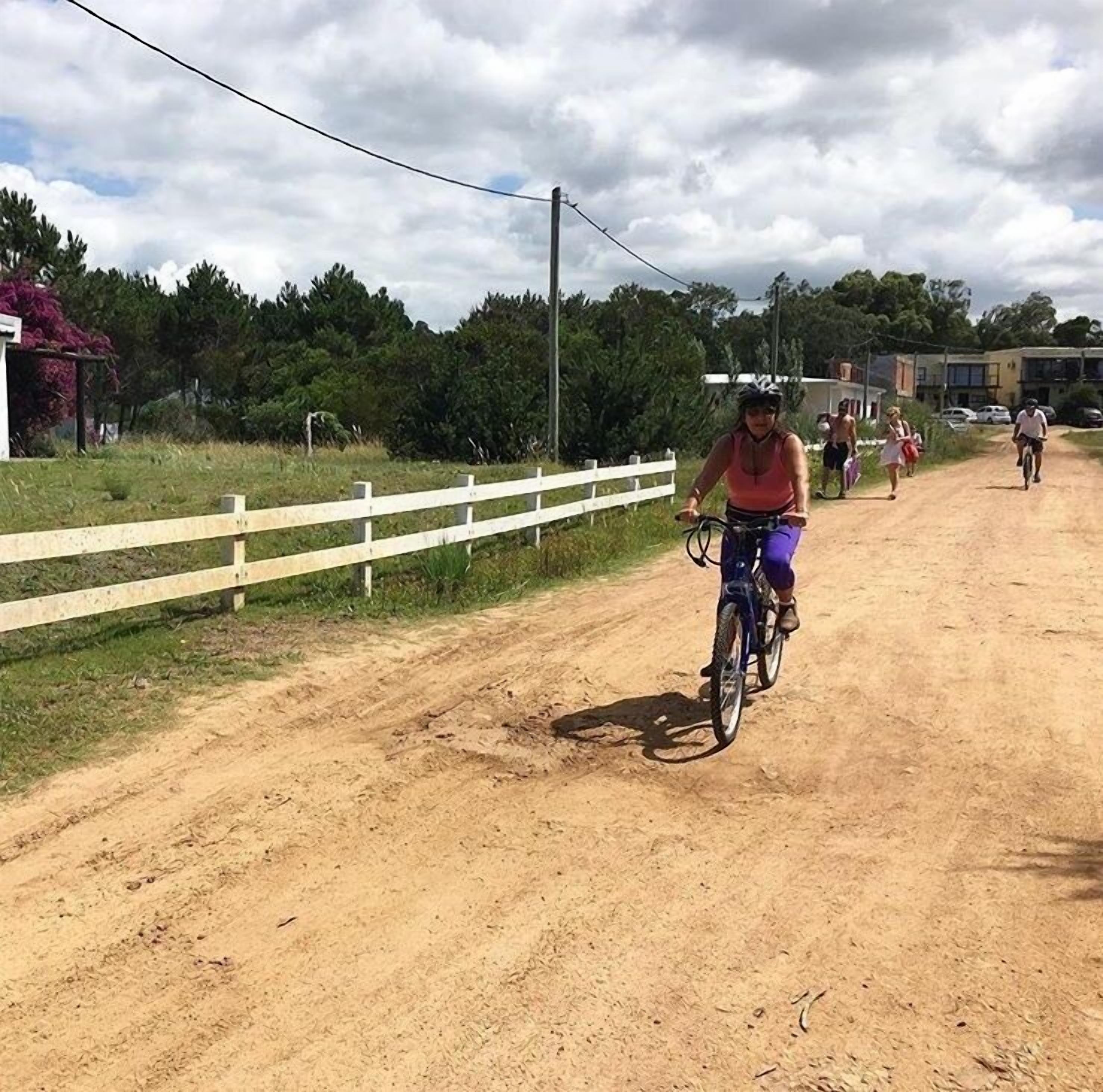 Camí de terra amb una tanca blanca a un costat i un ciclista al primer pla.