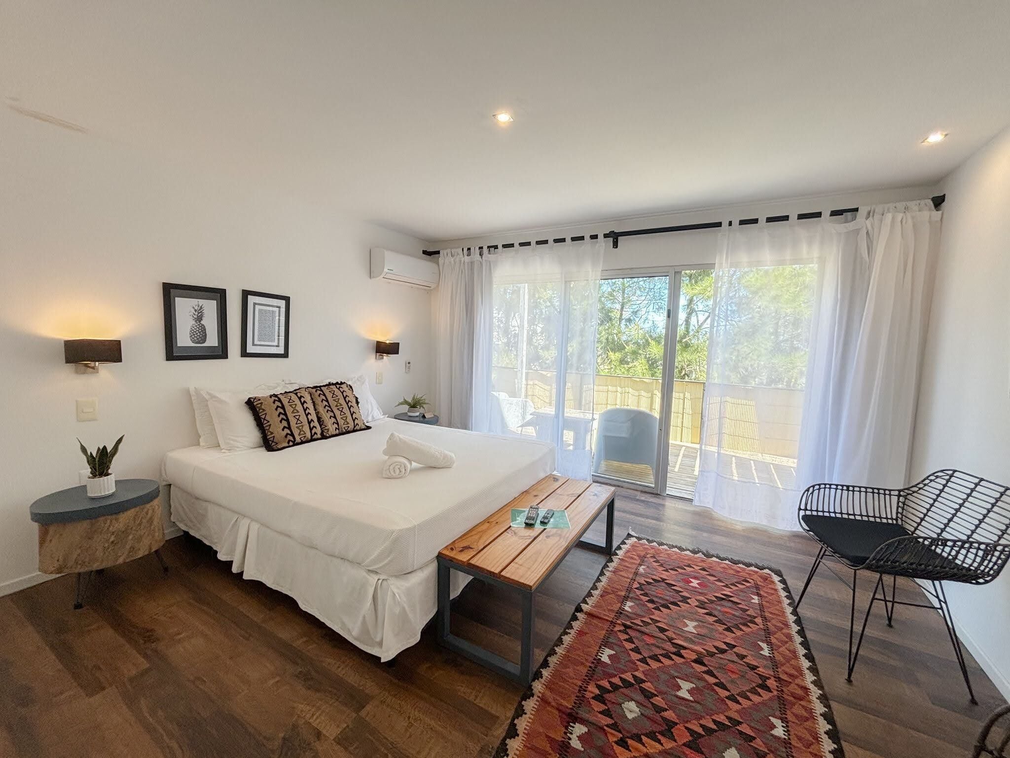 Une chambre à coucher comprenant un lit, des tables de chevet, un banc, une chaise et une vue sur l’extérieur.