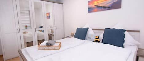 A neatly arranged bedroom with a large bed, a wardrobe with glass doors, and a painting on the wall.