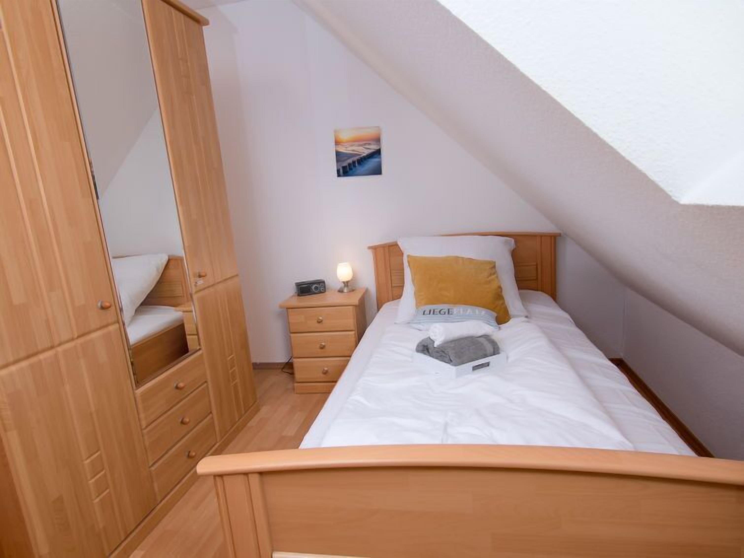 Een slaapkamer met een houten garderobe, een nachtkastje met een lamp en een bed met een kussen en dekbed.