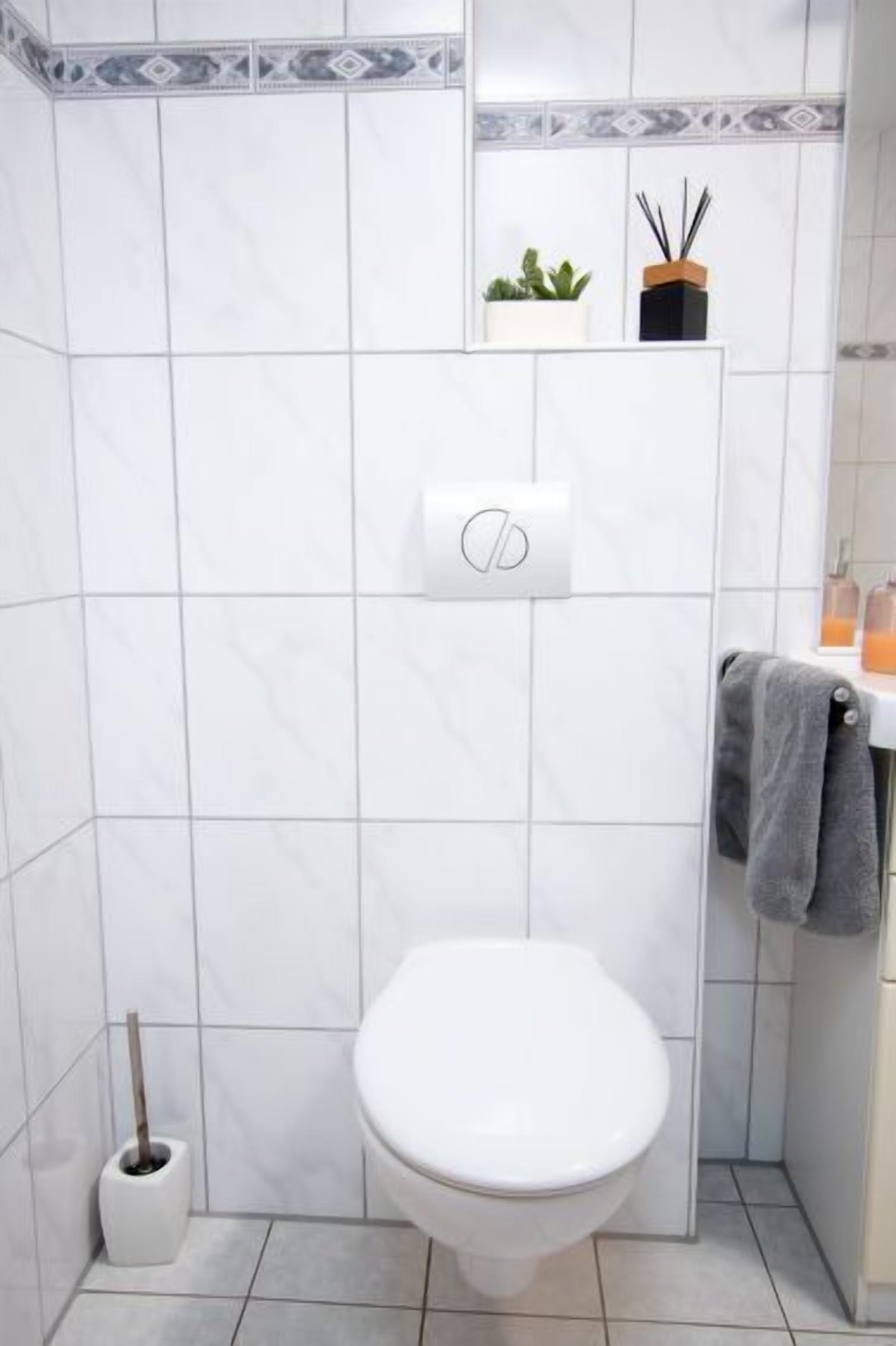 Een badkamer met een wit toilet, een toiletrolhouder, een kleine plant in pot en een handdoekrek.