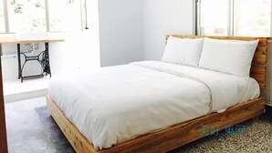 A bedroom with a wooden bed frame, white bedding, a sewing machine, and a large window. - Mayhow Donghe - Hostel (Donghe)