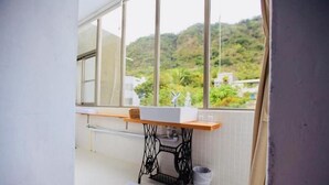 A small balcony with a sewing machine, a sink, and a view of a green hillside. - Mayhow Donghe - Hostel (Donghe)