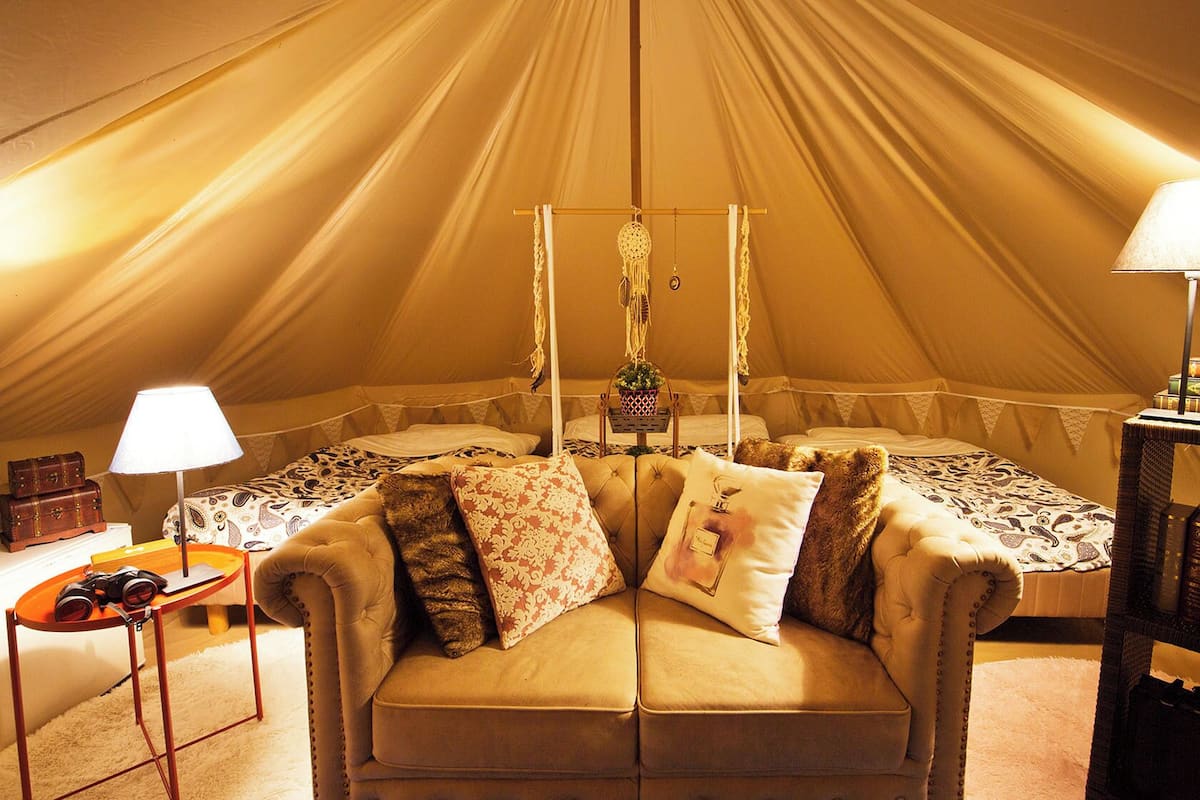 A tented accommodation with a sofa, lamps, and a small table with books and a plant.