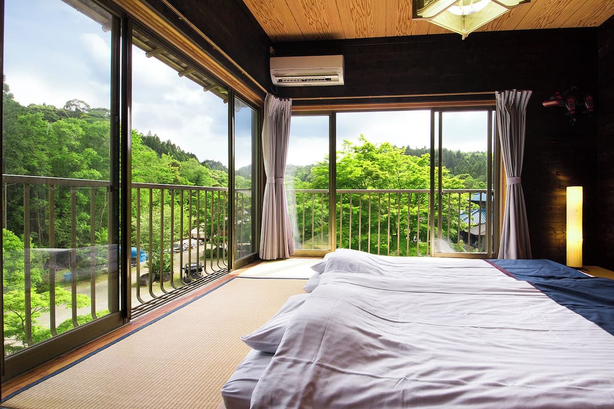 A bedroom with a large window, a bed, and a nightstand.