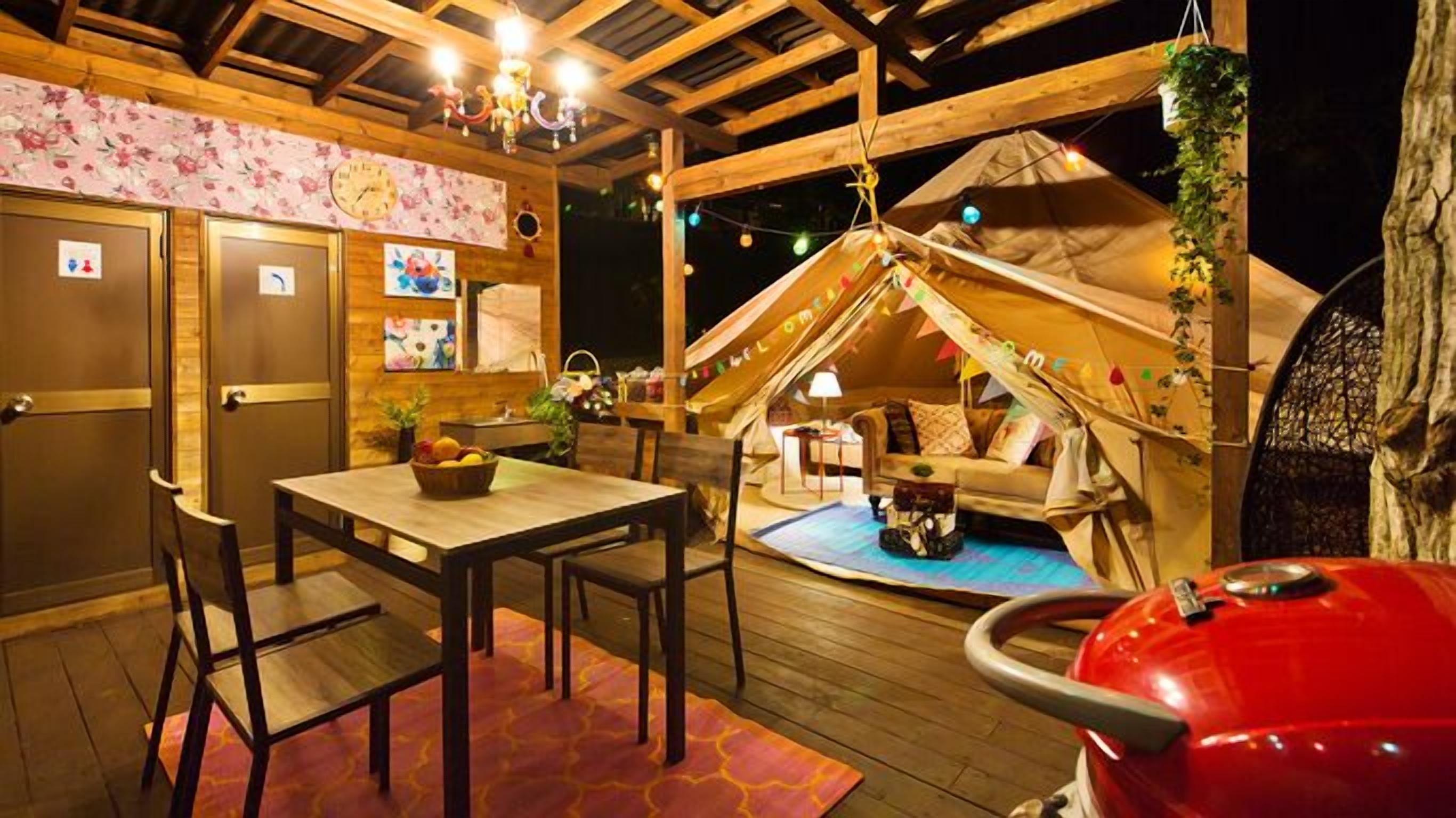 Un espacio al aire libre acogedor con mesa y sillas de madera, una parrilla roja y una estructura tipo tienda con un letrero de 'Welcome'.