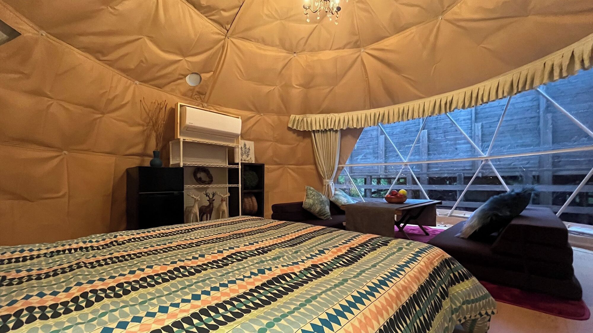 Una habitación con tienda de campaña, una cama, una mesita con un cuenco de fruta y una ventana con vista a un edificio.