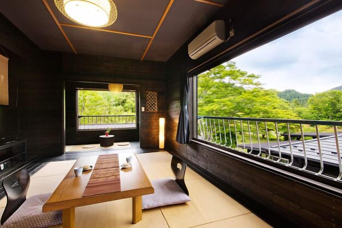 A room with a wooden table, a TV, a window with a view of greenery, and a balcony railing.