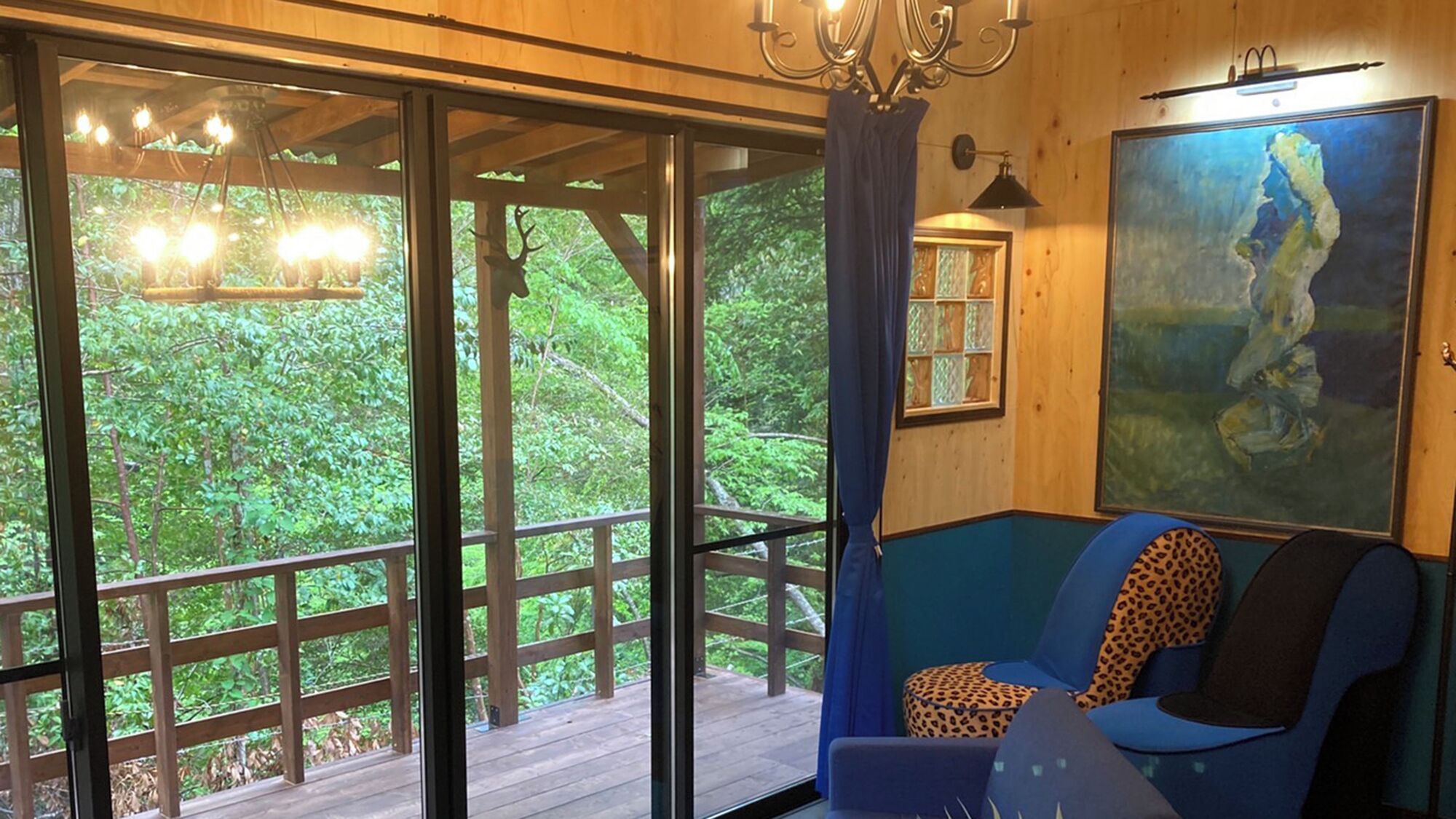 Una habitación con un ventanal grande, un sofá azul, un cojín estampado de leopardo y un cuadro en la pared.