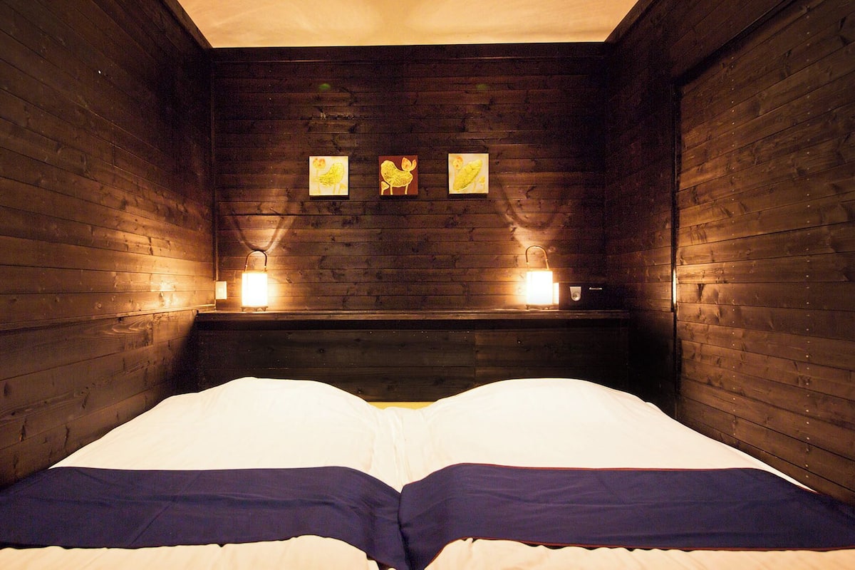 A wooden room with a bed, two wall-mounted lights, and three framed pictures.