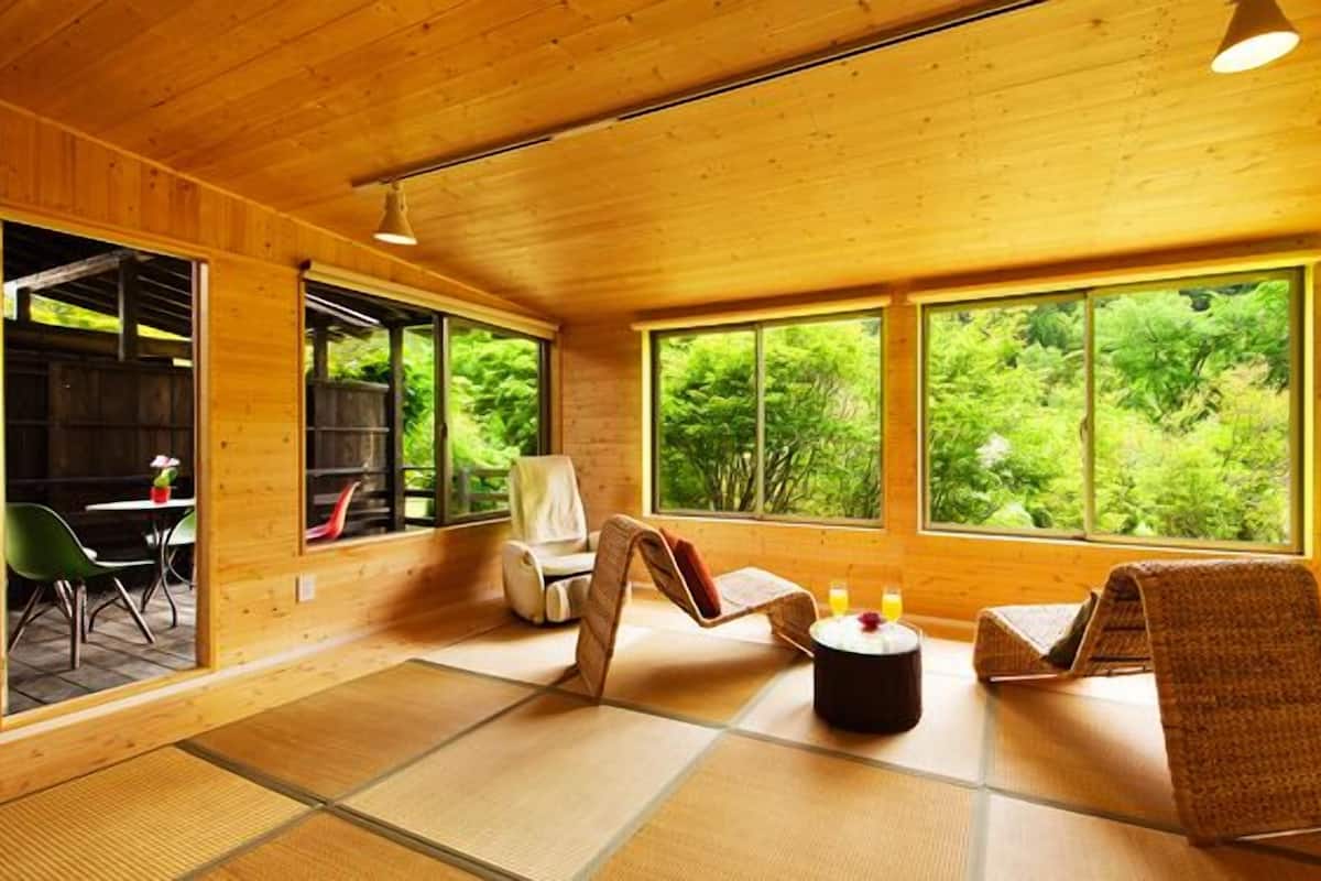 A wooden interior with tatami mats, a dining area, and large windows with a forest view.