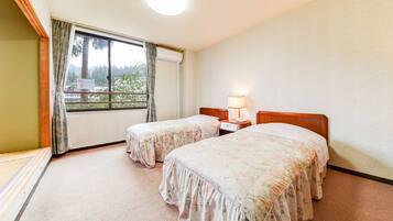 Habitación de hotel con dos camas, una ventana con cortinas, una mesita de noche con lámpara y un aire acondicionado instalado en la pared.