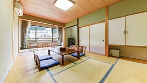Una habitación japonesa tradicional con suelo de tatami, una mesa baja con cojines, un televisor y puertas correderas.