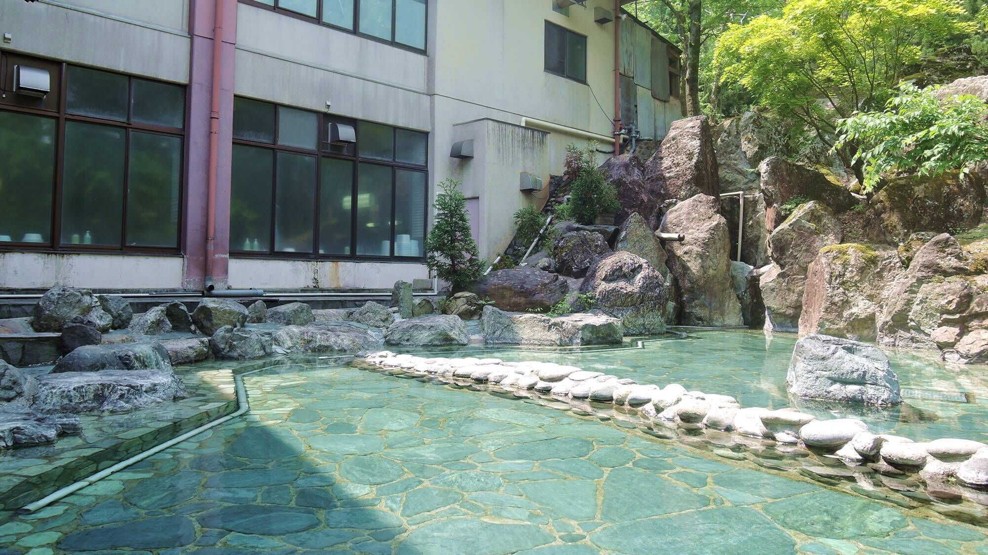 A traditional Japanese garden with a clear stone pond, large rocks, and a building with large windows.
