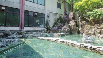 A traditional Japanese garden with a clear stone pond, large rocks, and a building with large windows.
