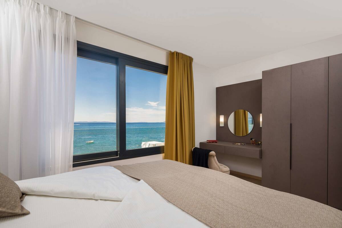 Une chambre d’hôtel avec un lit, une grande fenêtre donnant sur la mer, un miroir et une armoire.