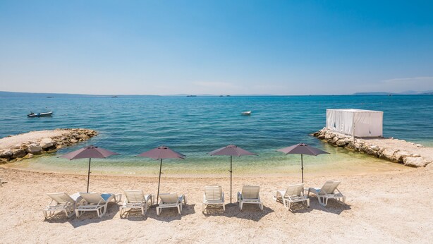 A beach with clear water, several lounge chairs, and umbrellas. - Villa Four Brothers Middle Floor (Podstrana)