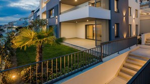 A modern multi-story residential building with balconies, a well-maintained garden, and a staircase leading to the entrance. - Villa Four Brothers Middle Floor (Podstrana)